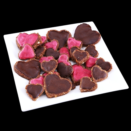 Vegan raw-food heart-shaped cookies served on a square plate isolated on black backgroundの写真素材