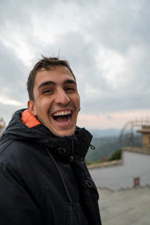 Young brunette man in jacket laughing out loud. Vertical view
