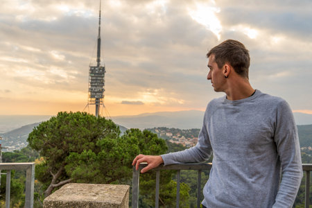 Young brown haired man looking at the electric tower behind him from the mountain during sunset