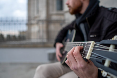 Close-up of a mans hands playing guitar sitting on the street. Music concept