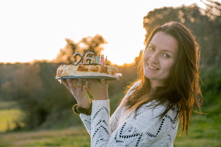Young woman in white sweater holding a birthday cake with misplaced candles. Copy spaceの写真素材