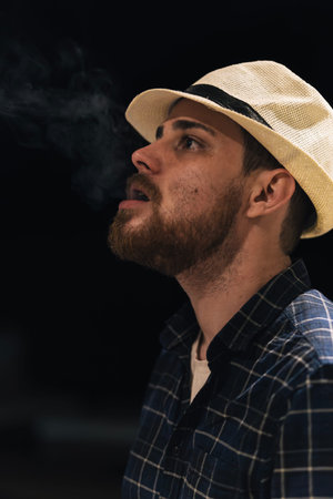 Vertical portrait of man blowing smoke out of his mouth with black background. Copy space