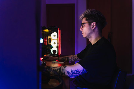 Young man with glasses and tattooed playing video games sitting in his gaming setup