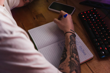 Detail shot of a tattooed graphic designer writing ideas in a notebook during his free time at home