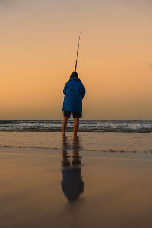 Lone fisherman fishing on the beach shore during sunsetの写真素材