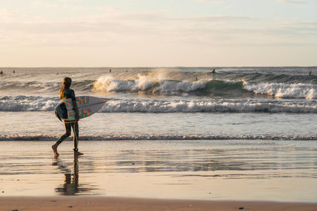 Surfer girl walking alone on the beach dressed in a military wetsuit at sunset