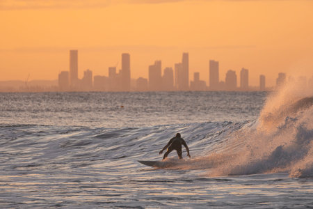 Surfer on top of his board in the sea with skyscrapers background during sunset. Gold Coast,...