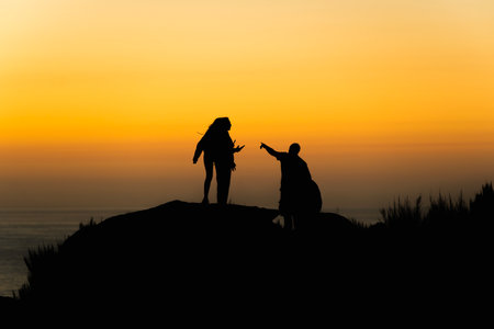 Silhouette of a group of friends enjoying the sunset on a cliff near the sea during summerの写真素材