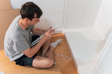 Young man assembling a cabinet sitting on the floor of his new homeの写真素材