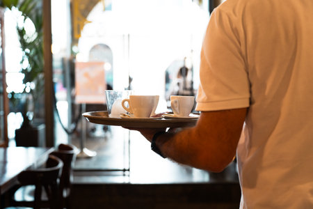 Waiter carrying coffees to a table with tray in one handの写真素材