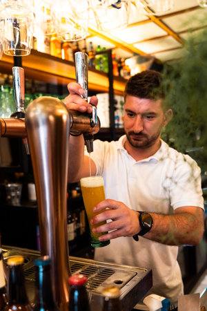 Waiter in white polo shirt filling a glass with beer at the restaurants pump. Verticalの写真素材