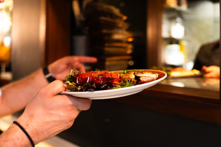 Close-up shot of a plate of Mediterranean salad held by a waiter in the restaurants kitchenの写真素材