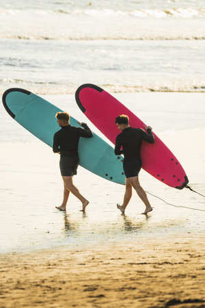 Two surfer friends walking along the beach with their surfboards before getting into the sea
