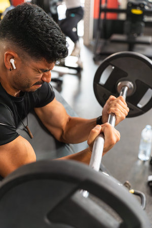 Latin man suffering while lifting the Z-bar in the gym