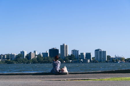 young woman sitting on the shore of the lake looking at the cityの写真素材