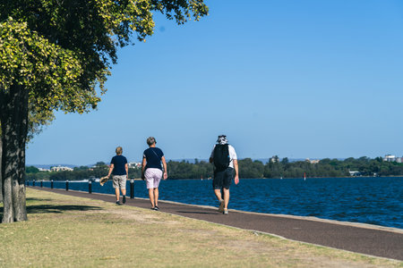 two women and a man of adult age walk along the shoreline of a lakeの写真素材