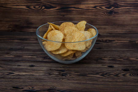 The glass bowl of potato chips sits on a wooden table.の写真素材