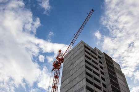 A crane near a house under construction against the blue sky.