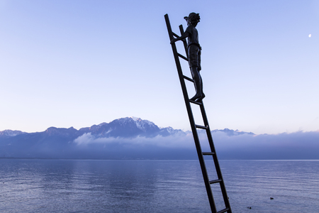SWITZERLAND, MONTREUX, DECEMBER, 28, 2015 - Bronze statue of boy on the stair of meet a sunrise on a background Swiss Alps and ashore of lake Geneva at Montreux.のeditorial素材
