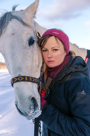 LATVIA, RIGA, DECEMBER, 08, 2016 -  Young beautiful woman petting her big white horse on a winter walk on the first snow in Riga, Latviaのeditorial素材