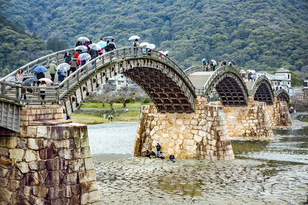 JAPAN, IWAKUNI, APRIL, 03, 2017 - Branches of cherry blossoms against the background of the Old Kintai Bridge, unique wooden arch bridge on stone pillars, spanning a river Nishiki in the city of Iwakuni, at Yamaguchi Prefecture, Japan.のeditorial素材