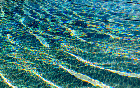 Waves of blue transparent water in swimming-pool with sunlight rays reflections