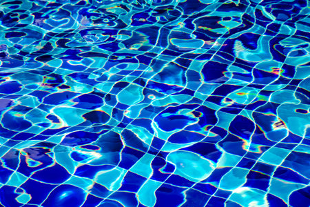 Blue transparent water in swimming-pool with sunlight rays reflections