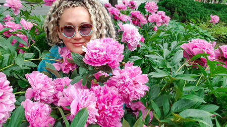 Nice girl with curly hair among fluffy pink peonies in the garden in Latviaの写真素材