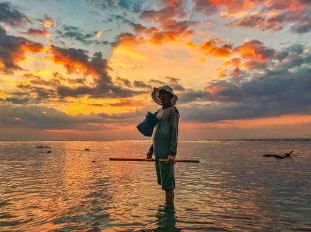 INDONESIA, BALI, AUGUST, 2019 - Oyster gatherer ashore of Indian Ocean at sunset in Baliのeditorial素材