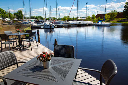 LATVIA, RIGA, AUGUST, 2021 - Wooden outdoor cafe terrace with summer furniture near the Daugava river in the small marine port. Riga. Latviaのeditorial素材