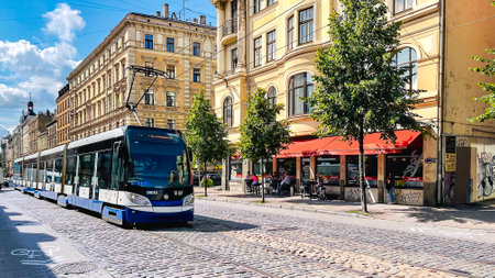 LATVIA, RIGA, AUGUST, 2021 - Modern low floor city tram on a city street lined with granite cobblestones in Riga, capital of Latviaのeditorial素材