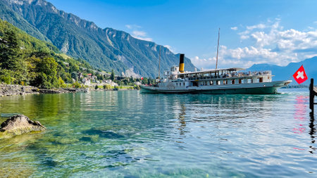 SWITZERLAND, MONTREUX, AUGUST 2021 - A pleasure ship with swiss flag is moored near the pier on Lake Geneva against the background of the Swiss Alps in Montreux. Switzerlandのeditorial素材
