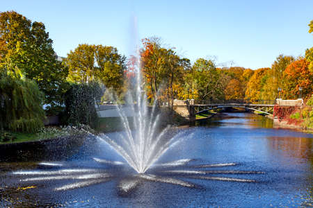 Riga city canal with fountain against the background of a bridge and a park with golden autumn foliage in Riga, capital of Latviaの写真素材