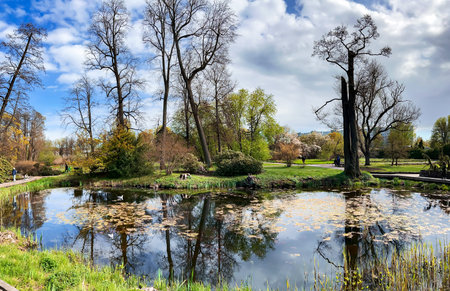 LATVIA. RIGA, APRIL, 2022: A small picturesque lake among trees and flowers in the Riga Botanical Garden, Latvia. Favorite place of rest for residents of Riga and guests of the cityのeditorial素材