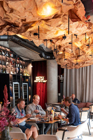 LATVIA, RIGA, AUGUST, 2022: A company of friends met for lunch in a cafe with an interesting interior. Yellow accentric crinkled fabric ceiling.のeditorial素材