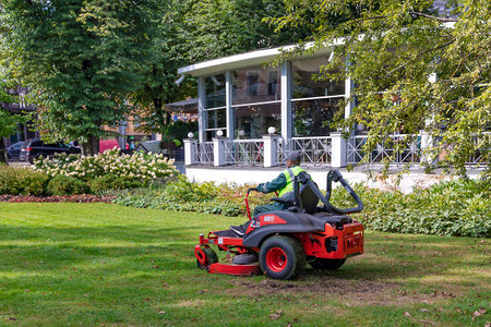 LATVIA, RIGA, SEPTEMBER, 2022: Man on a riding lawn mower that has grass stuck to the wheels in Riga city park. Season outdoor lawn maintenance.のeditorial素材