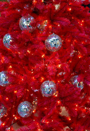 Red Christmas and New Year tree decorated with mirror balls and a light garland. Home decoration concept for Christmas.の写真素材