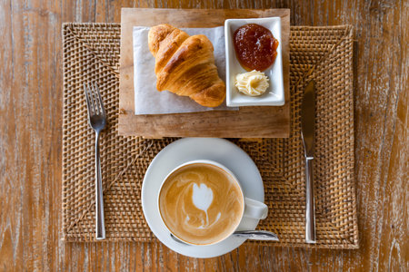 Balinese breakfast - cappuccino with croissant with butter and jam on a wicker tray in Ubud, Bali, Indonesiaの写真素材