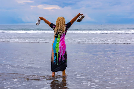 Beautiful young woman with long blonde hair in a colorful dress standing in the water on the...