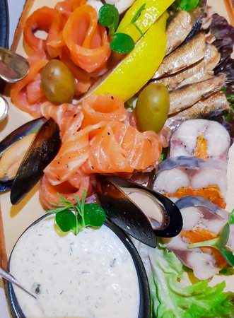 Fish platter with sliced salmon, mussels, smoked sprats, salted herring close-up. Garnished with herbs and lemon slices. Cold appetizer from valuable tasty species of marine fish.の写真素材