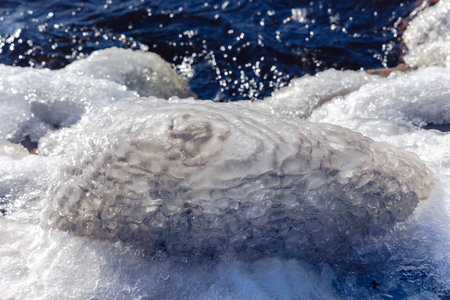 An iced stone with an interesting texture on a bright spring day on the embankment of the Daugava river in Riga, Latvia. Winter background.の写真素材