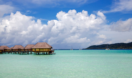 Overwater bungalows stretching out across the lagoon and a few catamarans in a quiet bay in Bora Bora island, Tahiti. Romantic honeymoon destination.の写真素材