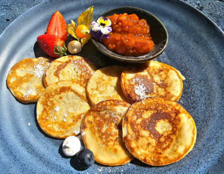 Freshly fried pancakes with cloudberry jam served on a blue dish on a bright sunny day closeup. Healthy morning breakfast with pancakes and fruits.の写真素材