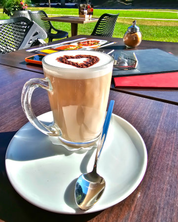 A large latte cup with a chocolate heart on the open veranda on a summer morning.の写真素材