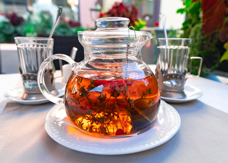 Glass teapot with herbal tea and cranberries and rays of light with faceted glasses in glass holders in the background. Delicious food close-up.の写真素材