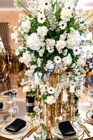 Large luxurious wedding bouquet of white flowers on a festive table with beautiful dishes and candles in a restaurant close-up. The names of the guests are written on black napkinsの写真素材