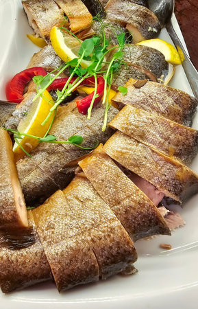 Chunks of cold smoked rainbow trout with lemon slices and fresh micro greens close-up