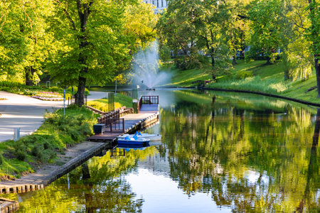 A clean and calm Riga city canal surrounded by trees with spring foliage and a wooden pier for pleasure boats, Riga. Latvia.の写真素材