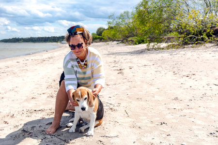 A pretty woman in sunglasses walks with her dog Beagle breed on the Baltic Sea coast in Latvia. The concept of friendship with pets.の写真素材