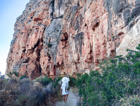 A girl in a white dress and hat hikes near the Rocky Cliffs at Cala La Granadella, Javea, Costa Blanca, Alicante Province, Spainの写真素材